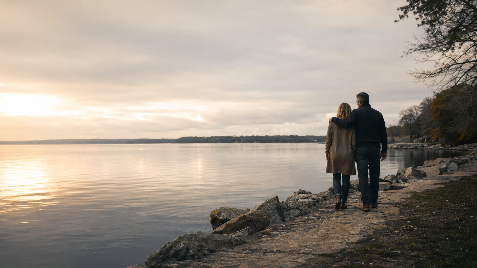A married couple walking together beside calm water